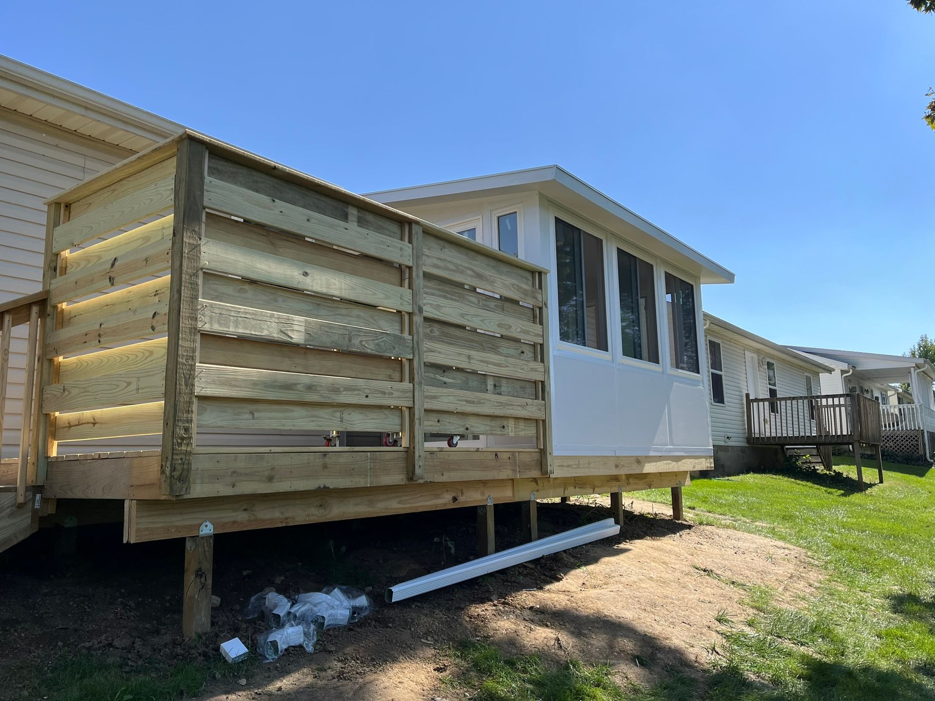 Wooden deck with privacy screen next to a white-walled sunroom and grass lawn.