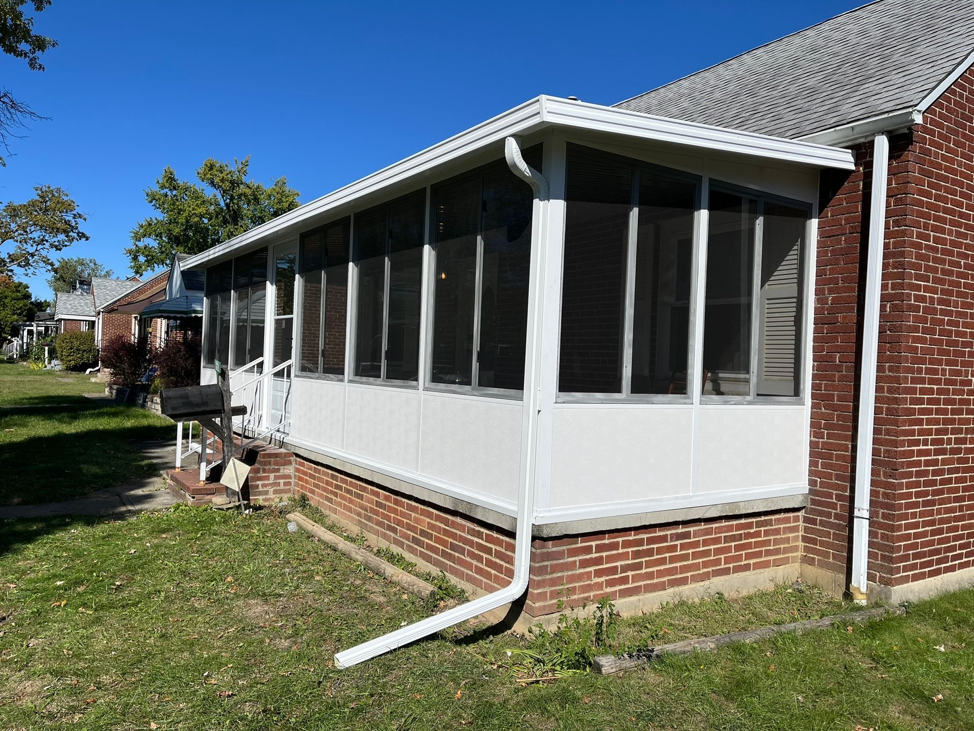 Screened-in porch attached to a brick house, white trim, green lawn, clear blue sky.