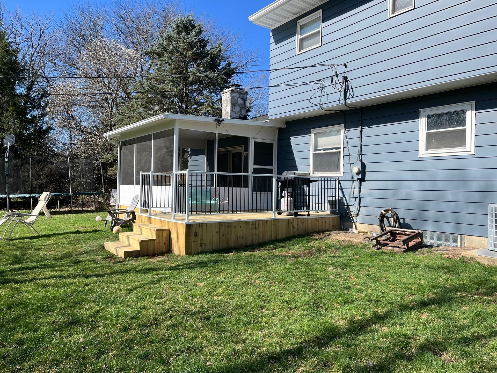 Backyard with a light wood deck and screened porch attached to a blue house with green grass.