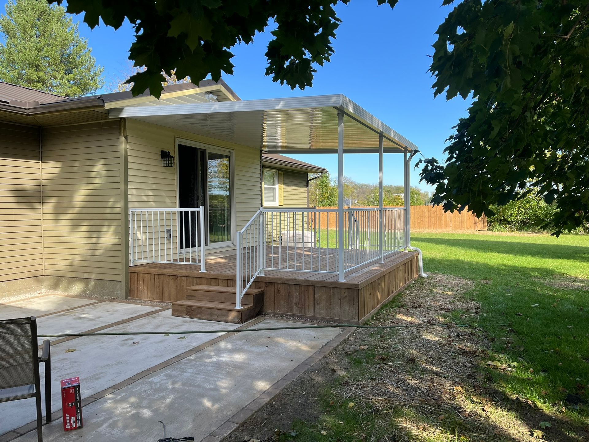 Deck with a clear roof attached to a house with white railings, and a concrete patio.
