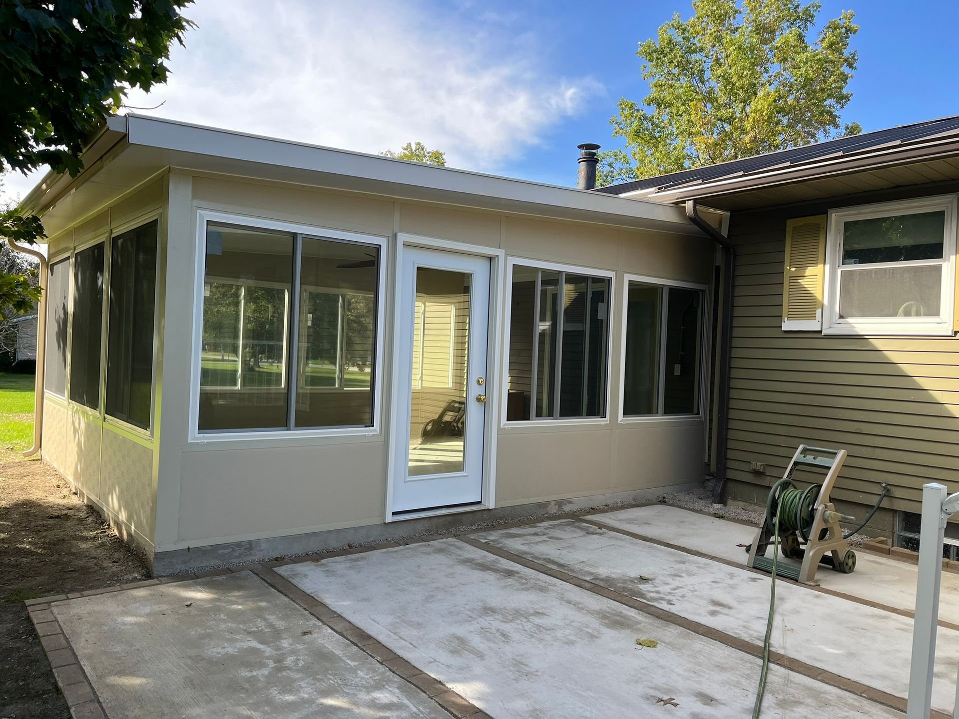 Sunroom addition with light tan siding, white trim, glass windows, and a concrete patio.