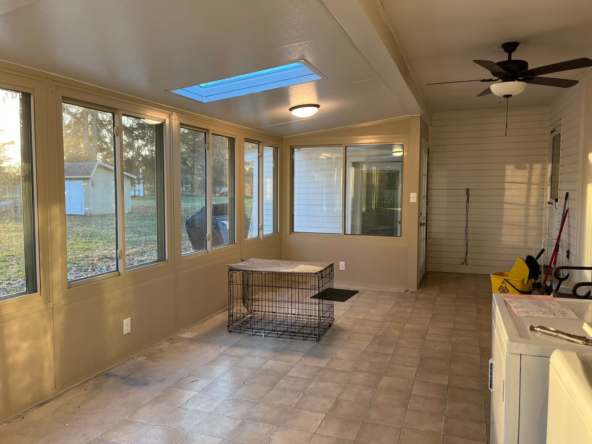 Sunroom with large windows, skylight, and tiled floor. A metal dog crate sits in the center.