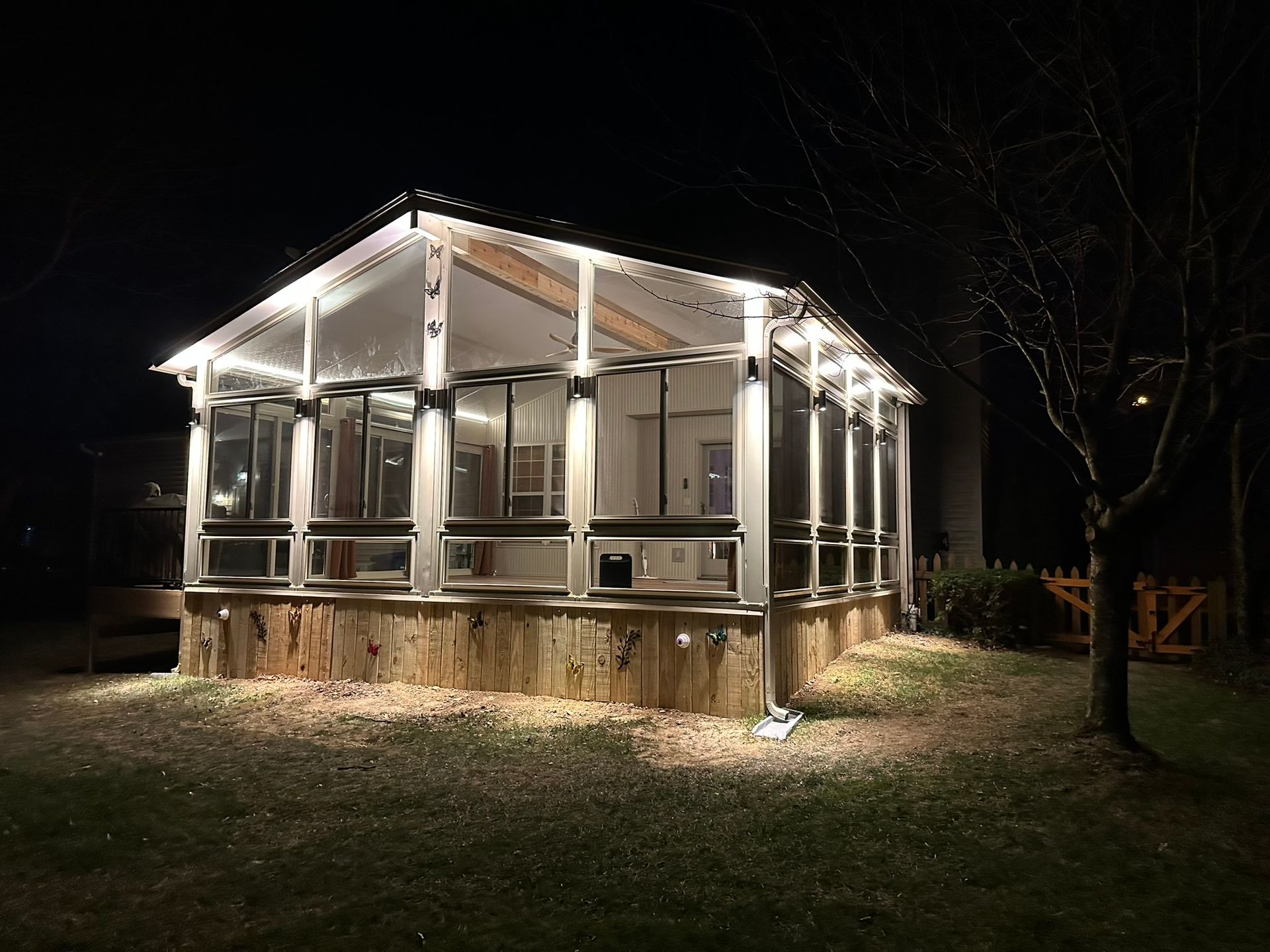 Lit-up screened-in porch at night, with fairy lights outlining the structure. Wooden siding on the lower half.