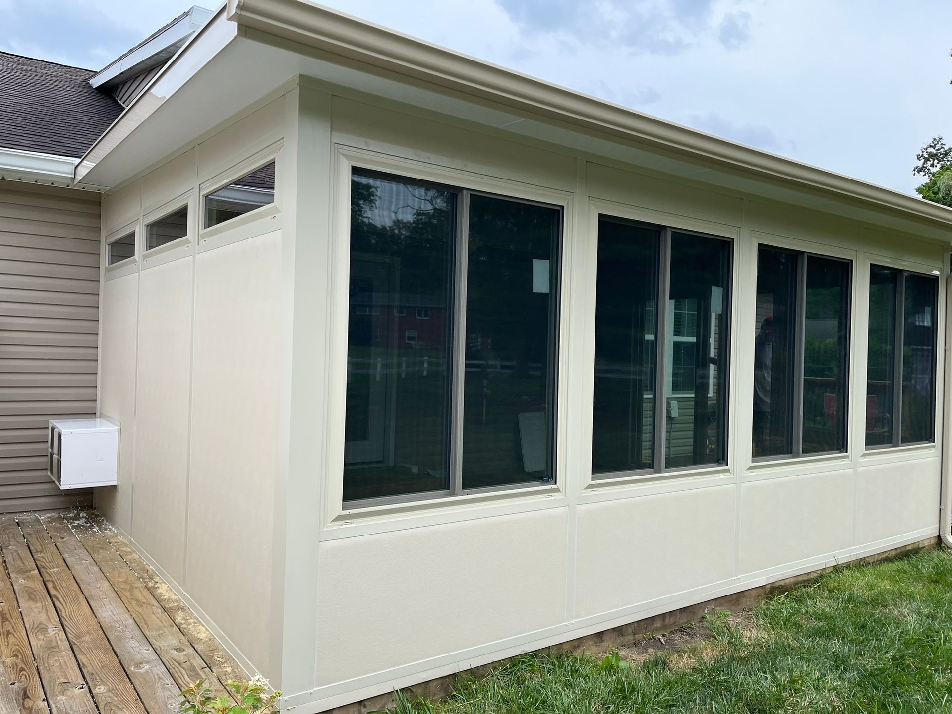 Beige sunroom addition with multiple large windows, attached to a house with wooden deck.