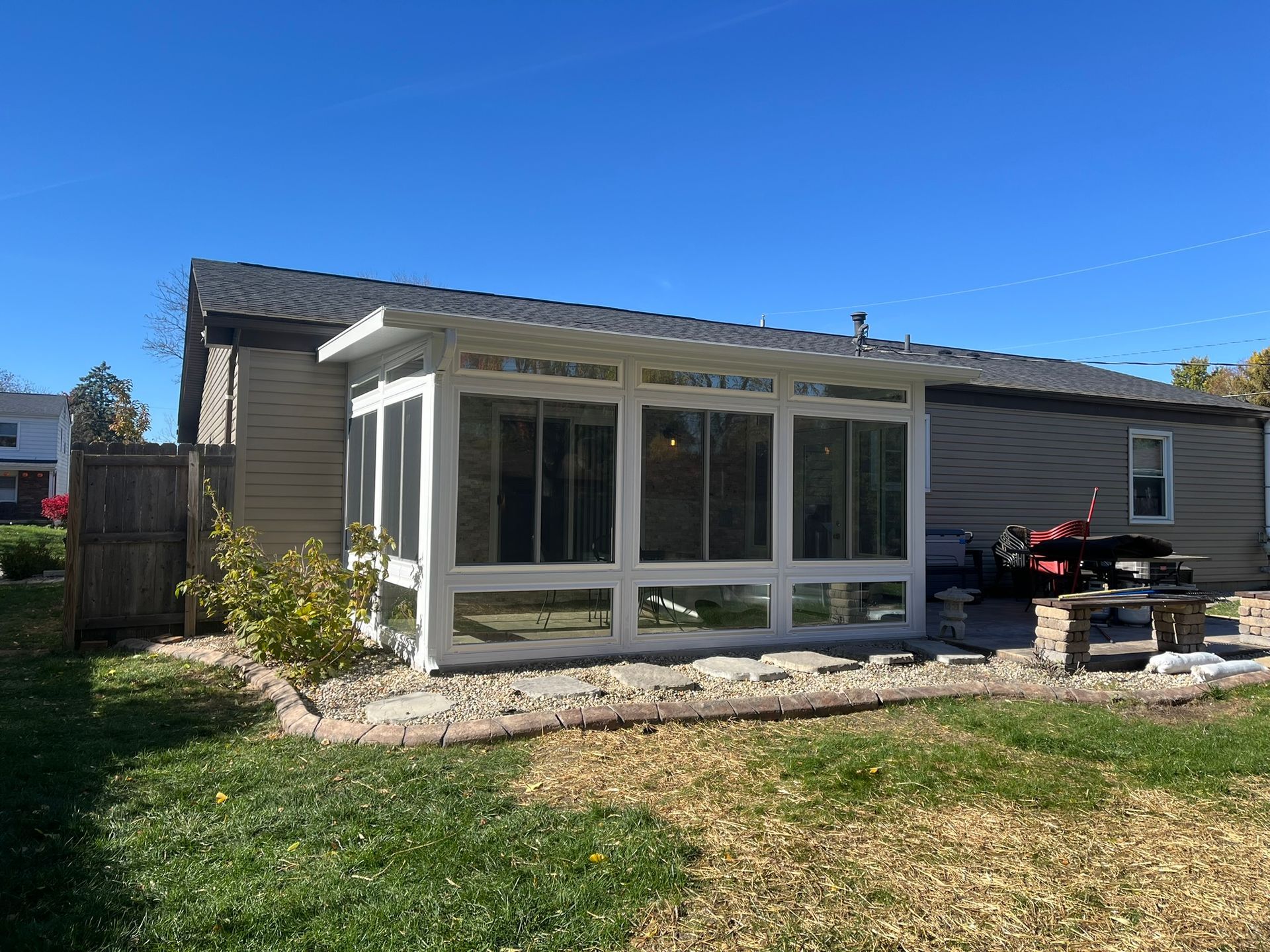 Sunroom addition on a house with white trim, lots of windows, and a patio area.