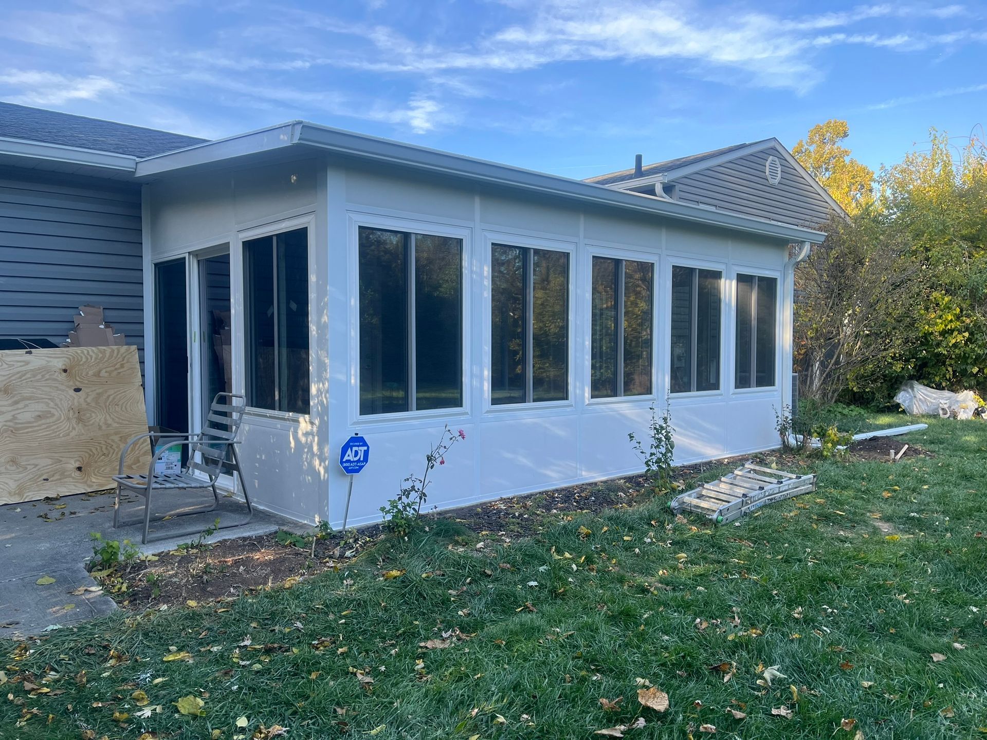 White sunroom attached to a house with large windows, set in a grassy backyard.