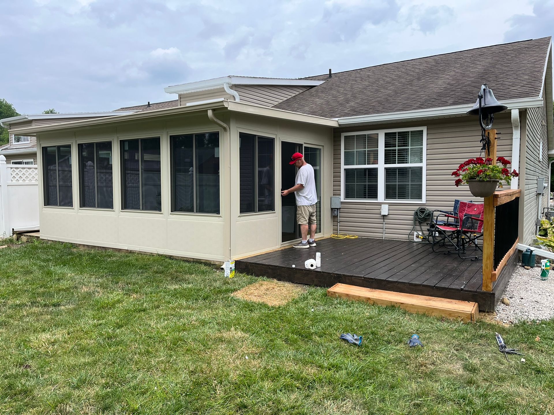 Man standing in doorway of sunroom, looking out at a backyard with a deck.