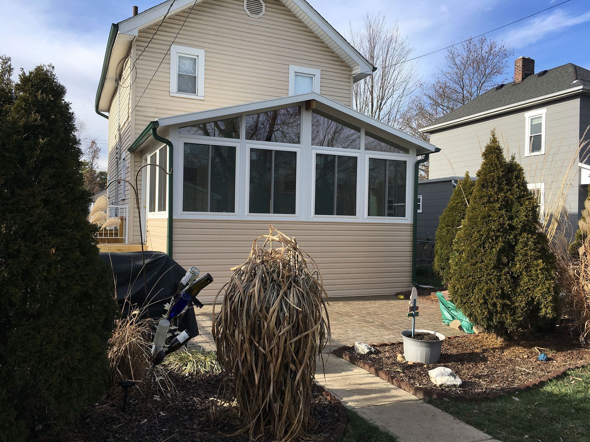 Two-story house with a sunroom addition, beige siding, and surrounding yard with plants.