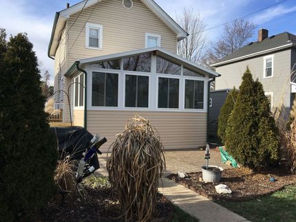 Two-story house with a sunroom addition, beige siding, and surrounding yard with plants.