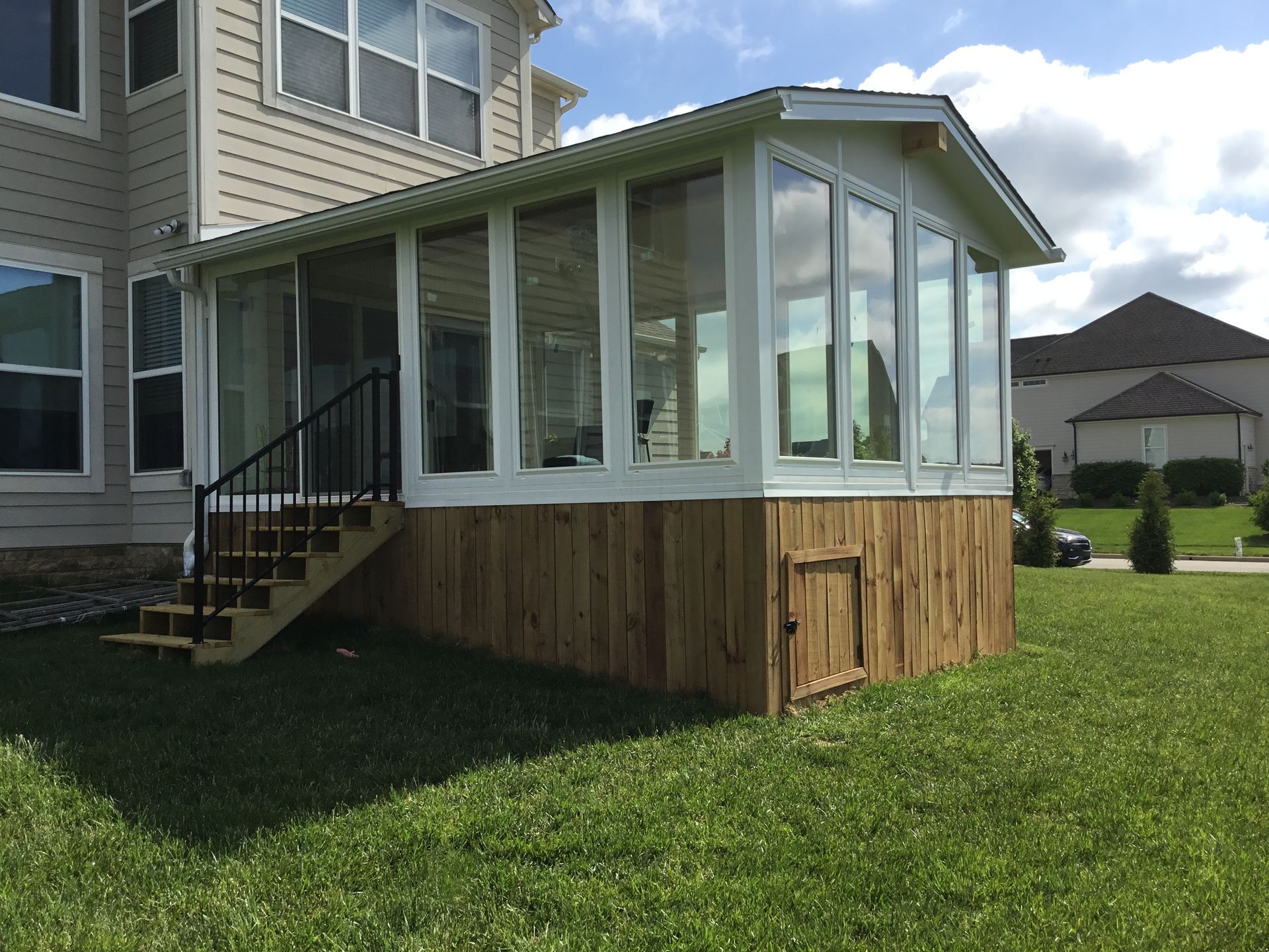 A sunroom with white-framed windows and wood siding attached to a house with stairs leading down to a grassy yard.