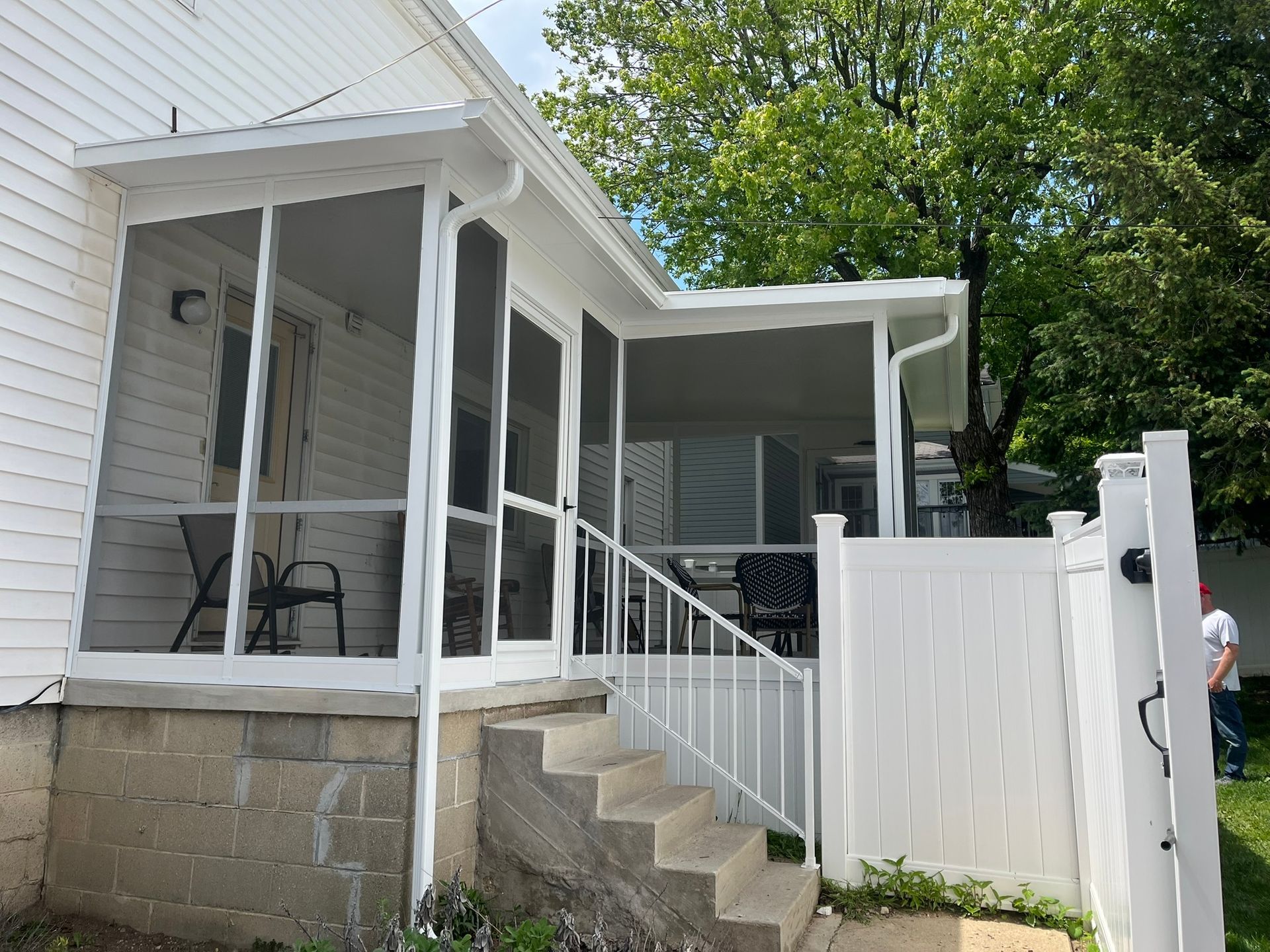 Screened-in porch attached to a white house with concrete steps and white railing.