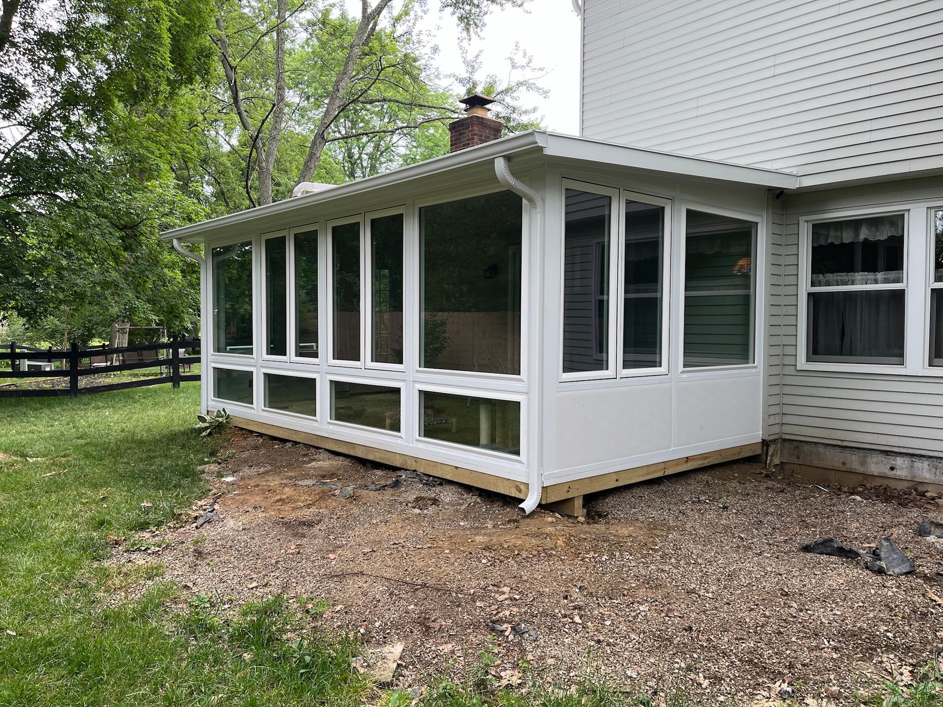 White screened-in porch addition with numerous windows, attached to a house with a gravel base.