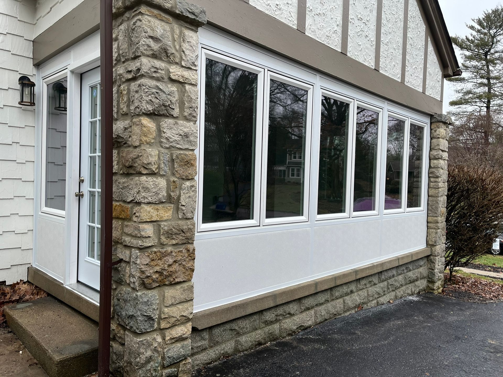 Stone and white-paneled enclosed porch with a door and windows.