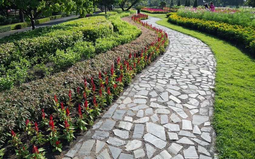 A stone walkway in a park surrounded by flowers and bushes.