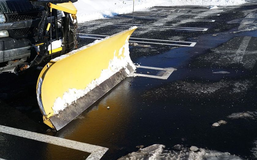 A yellow snow plow is plowing snow in a parking lot