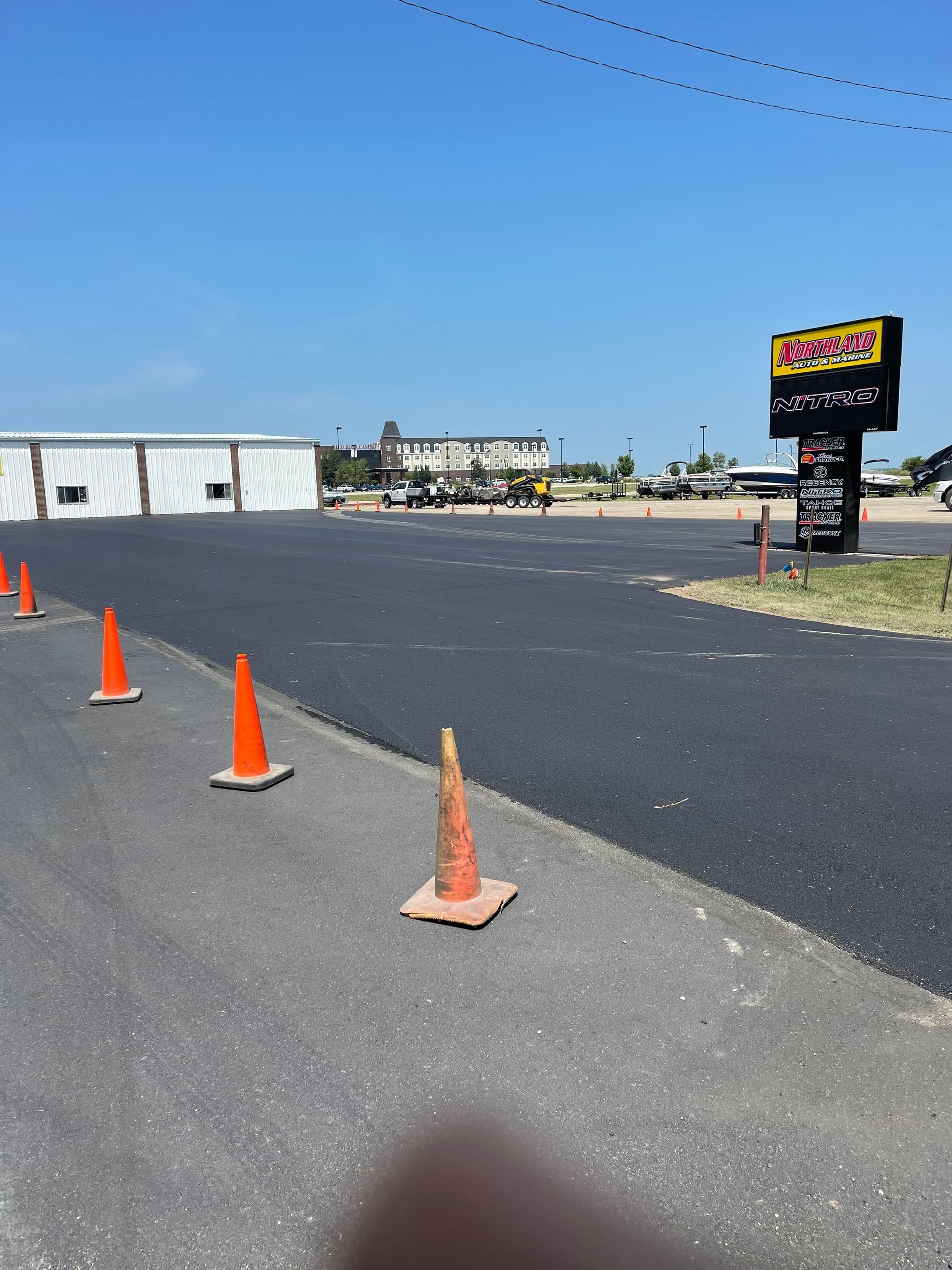 Freshly paved asphalt with orange cones. A sign for a business stands in the background on a sunny day.