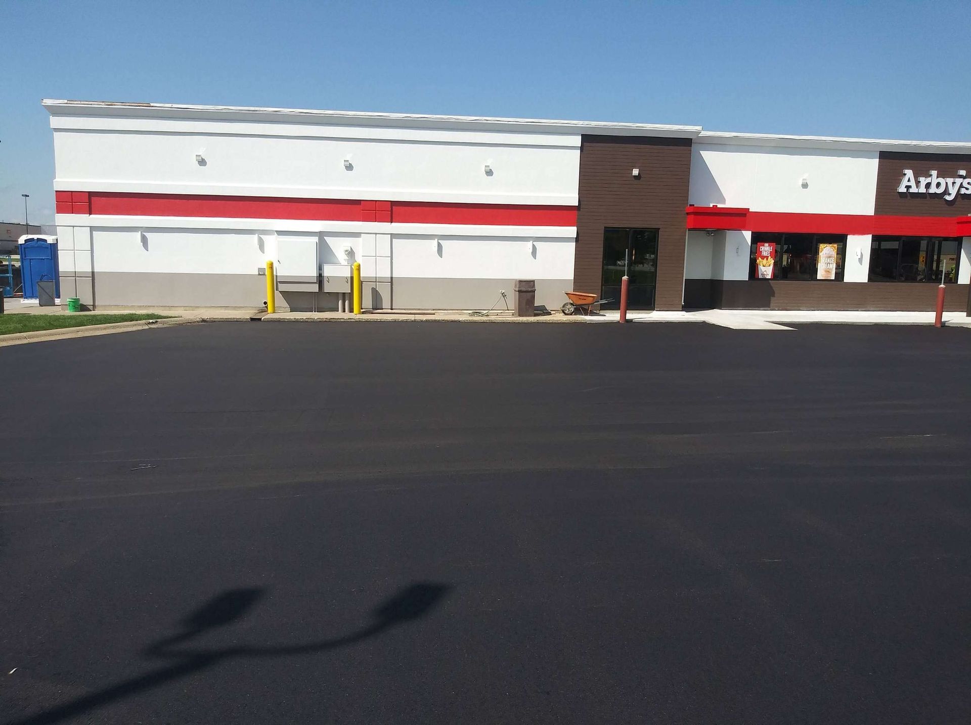 Exterior of an Arby's restaurant with a red stripe and new black asphalt parking lot on a sunny day.