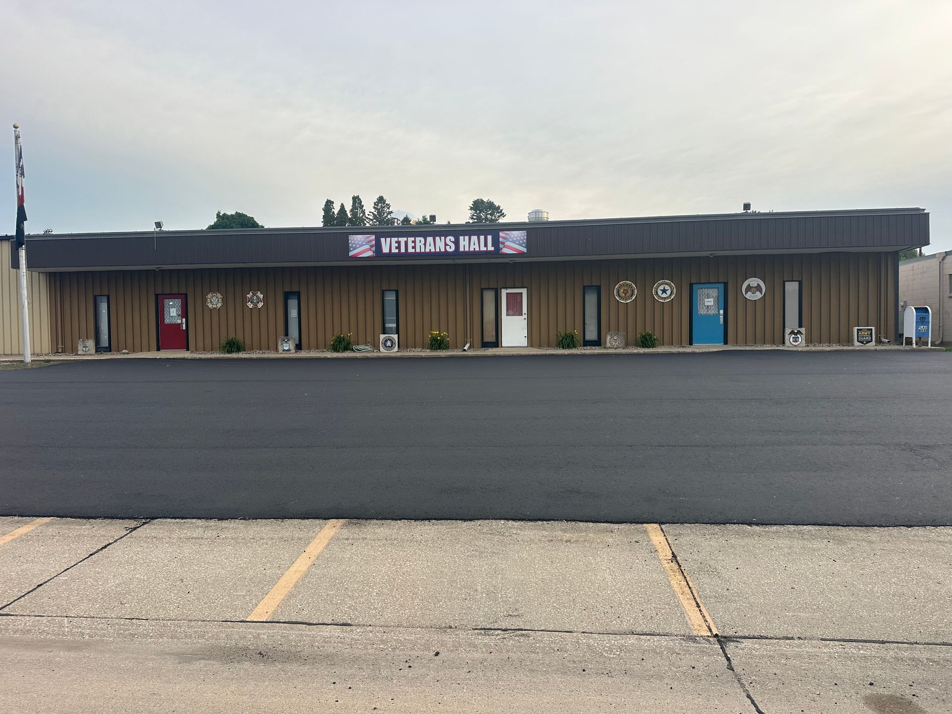 Veterans Hall building with tan siding, several doors, and parking lot.