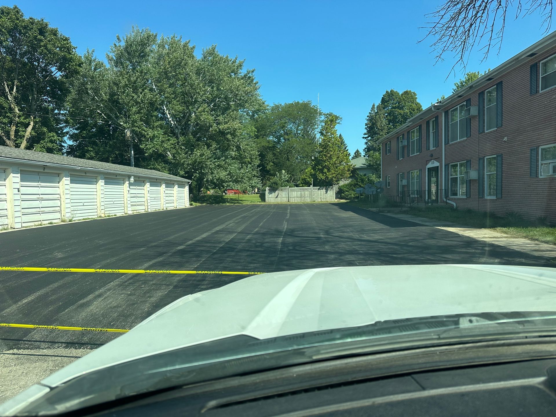 View from a car windshield of a newly paved parking lot, apartment building, and garage.
