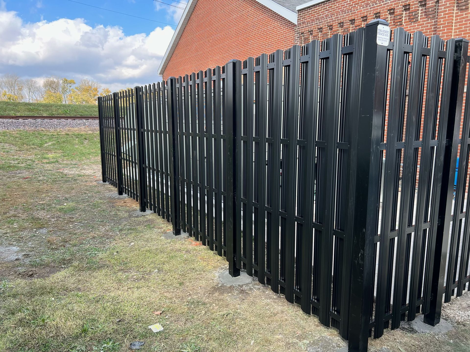 A black fence is sitting in the grass in front of a brick building.