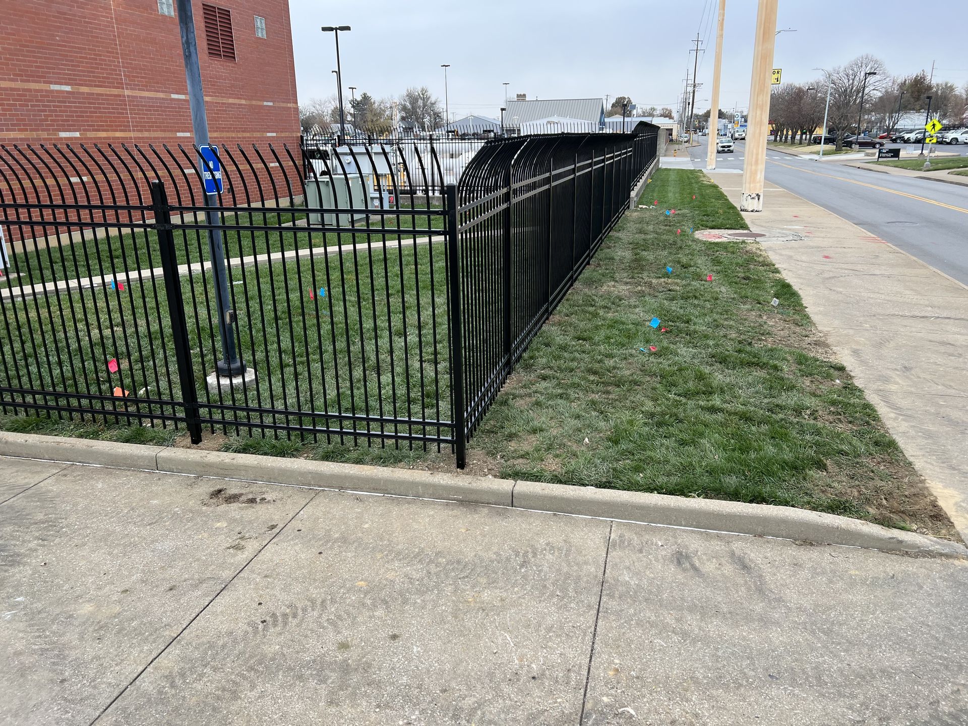 A black fence surrounds a grassy area next to a sidewalk.