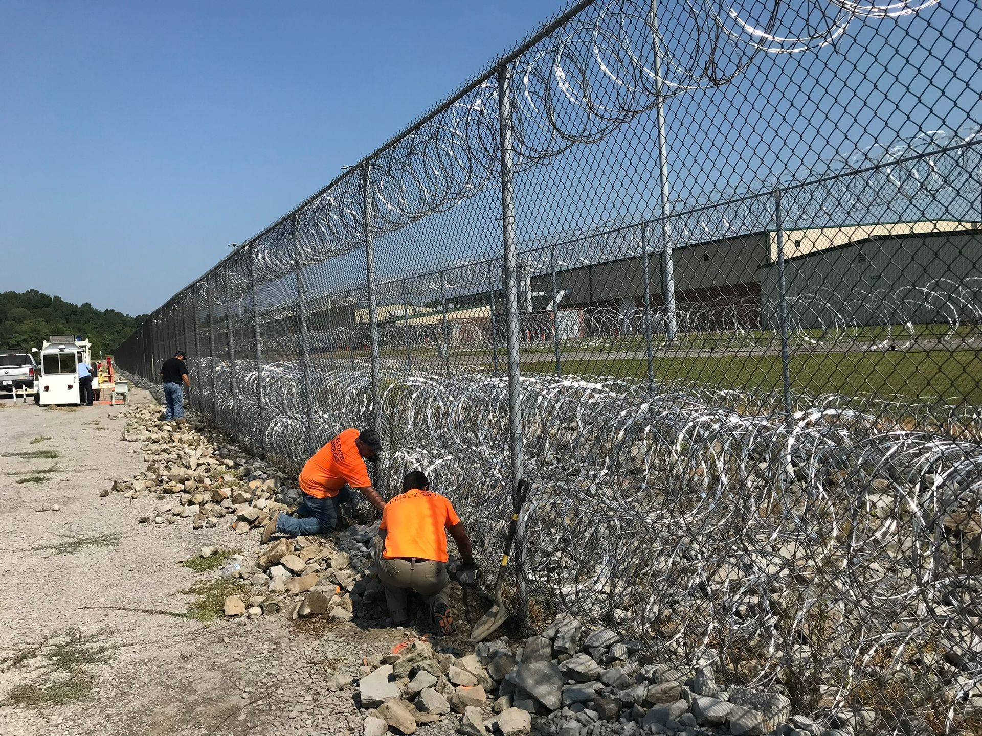 Two men are working on a chain link fence.