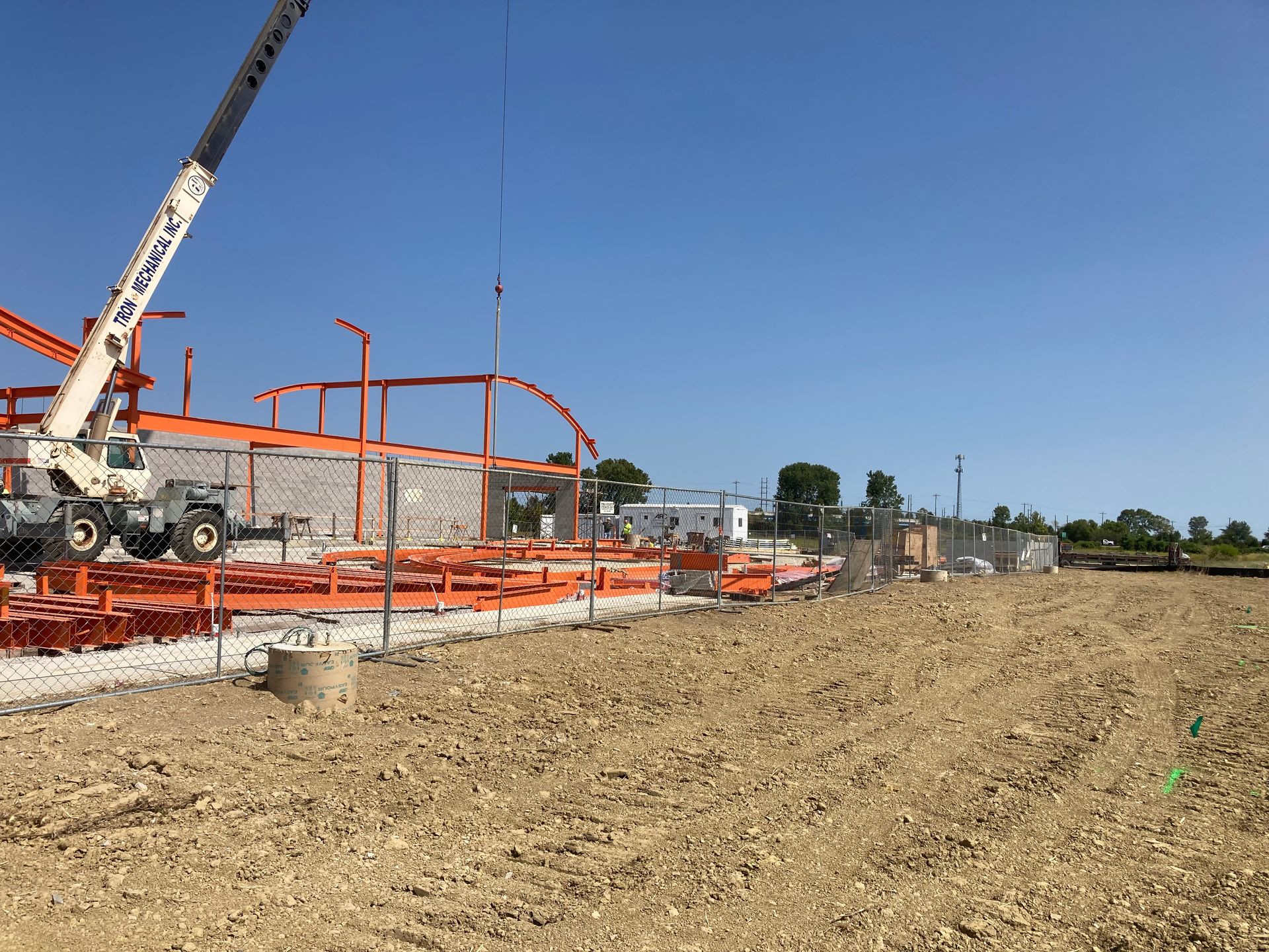 A crane is lifting a metal structure in a dirt field.