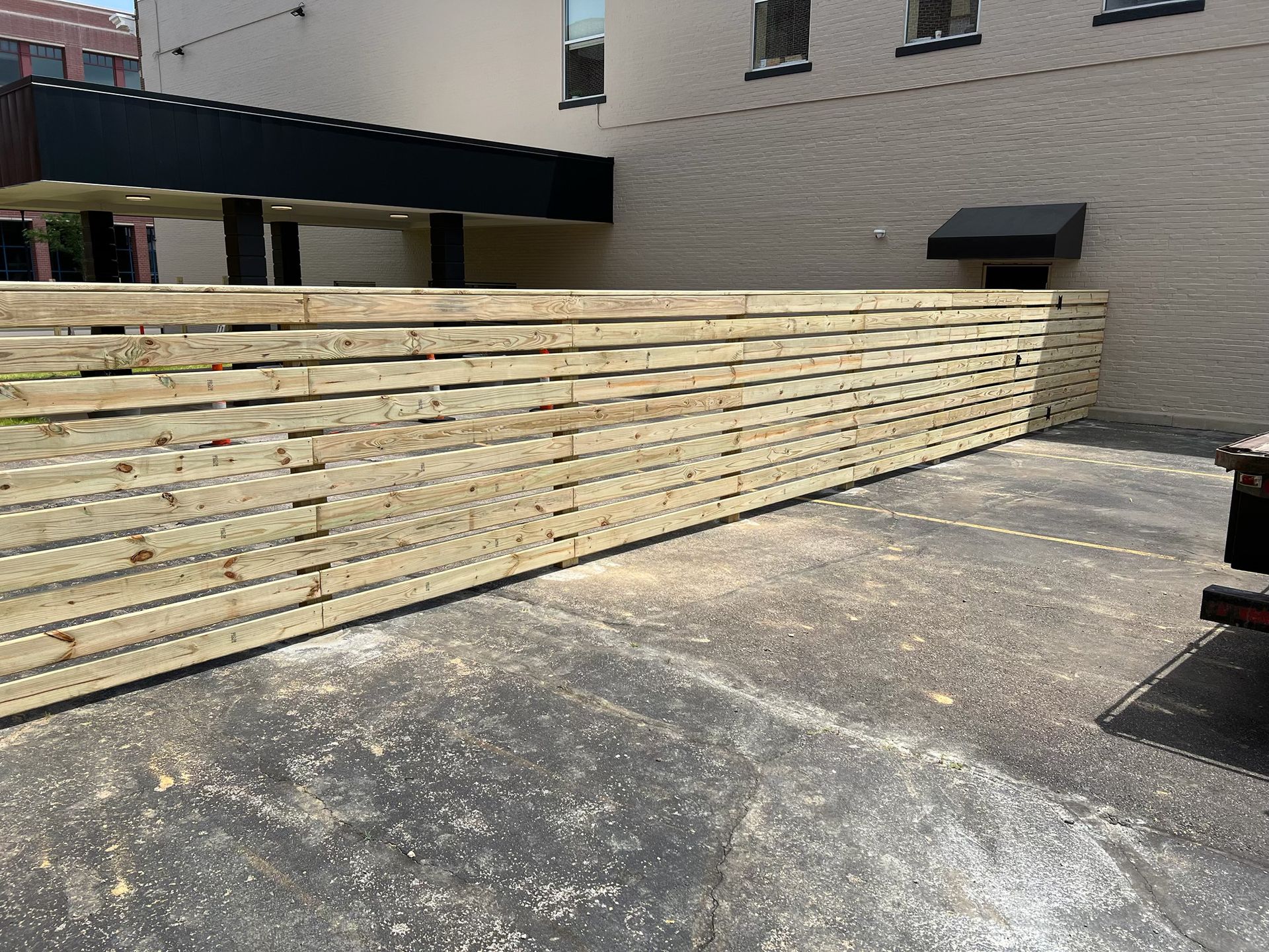 A large wooden fence is sitting in a parking lot next to a building.
