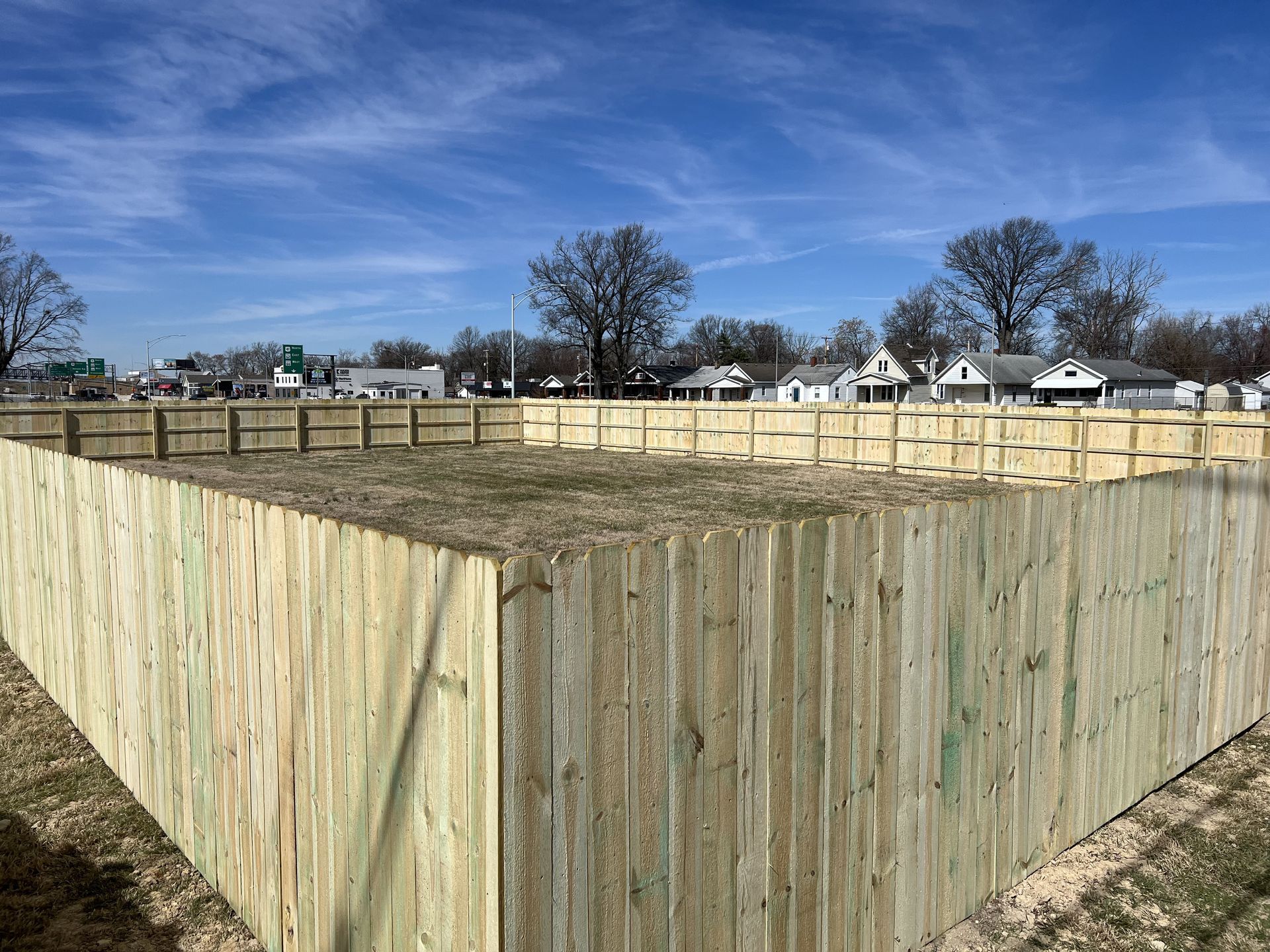 A wooden fence is surrounding a field with houses in the background.