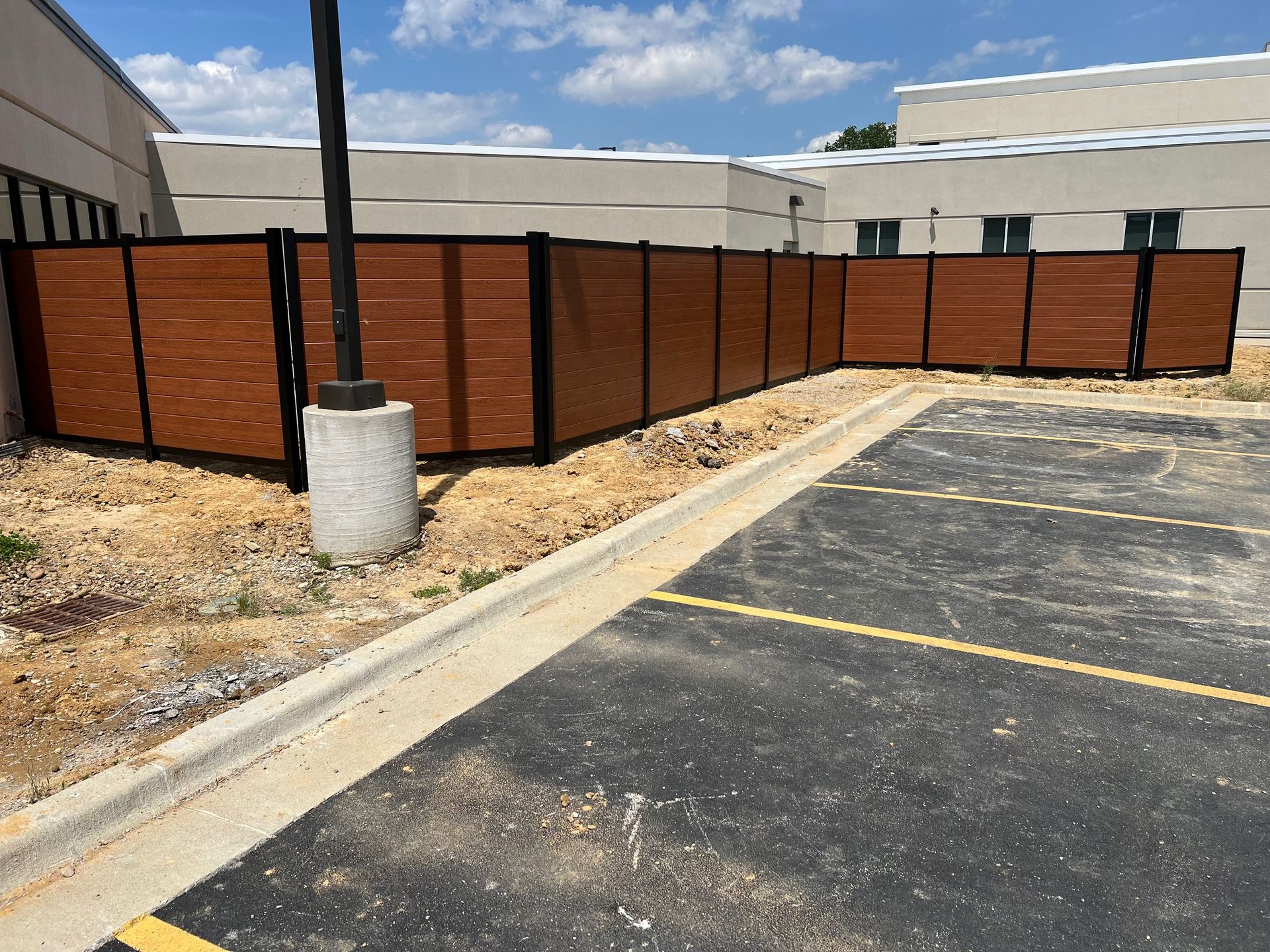 A wooden fence is surrounding a parking lot in front of a building.