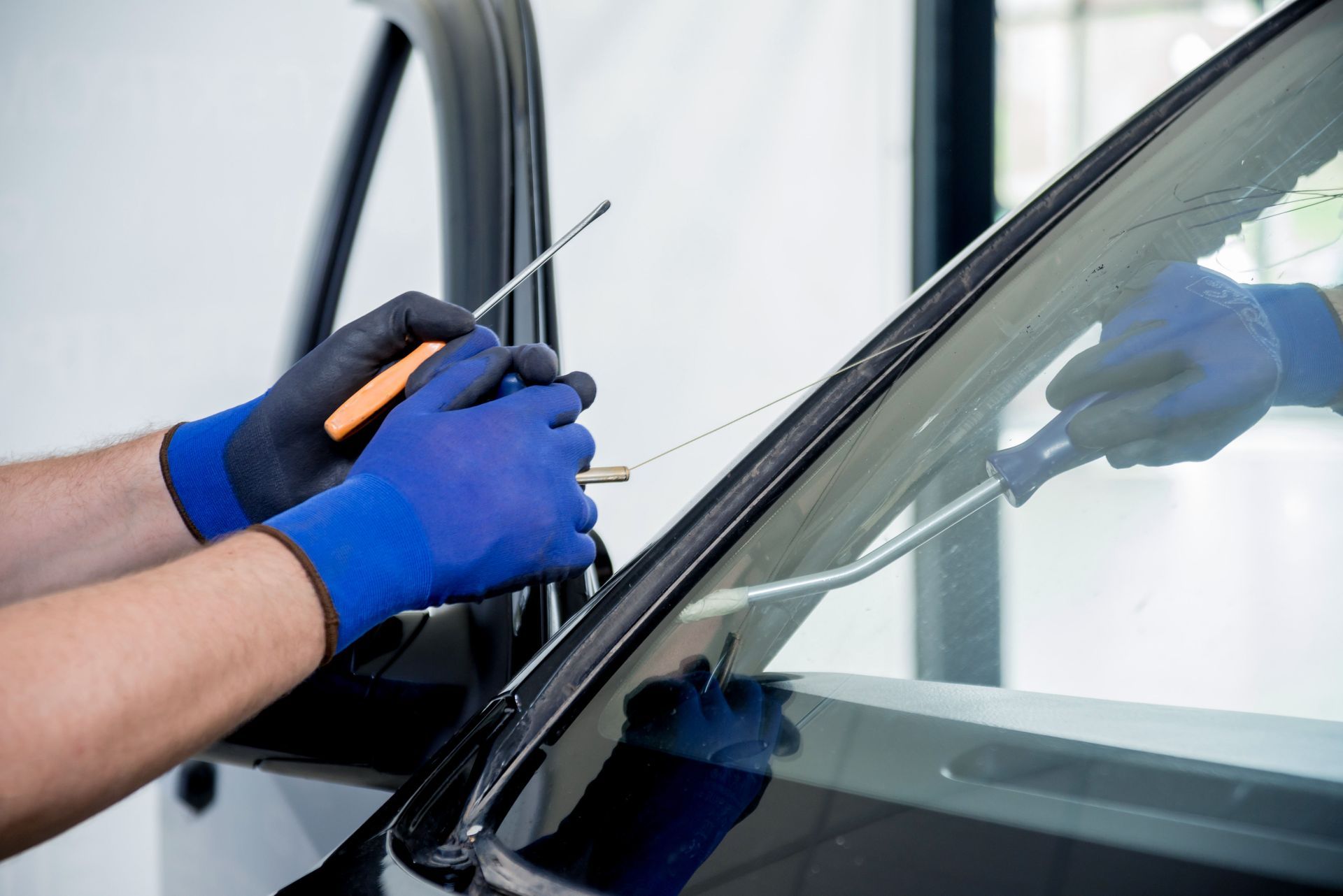 Close-up of gloved hands using specialized tools to remove a car windshield.