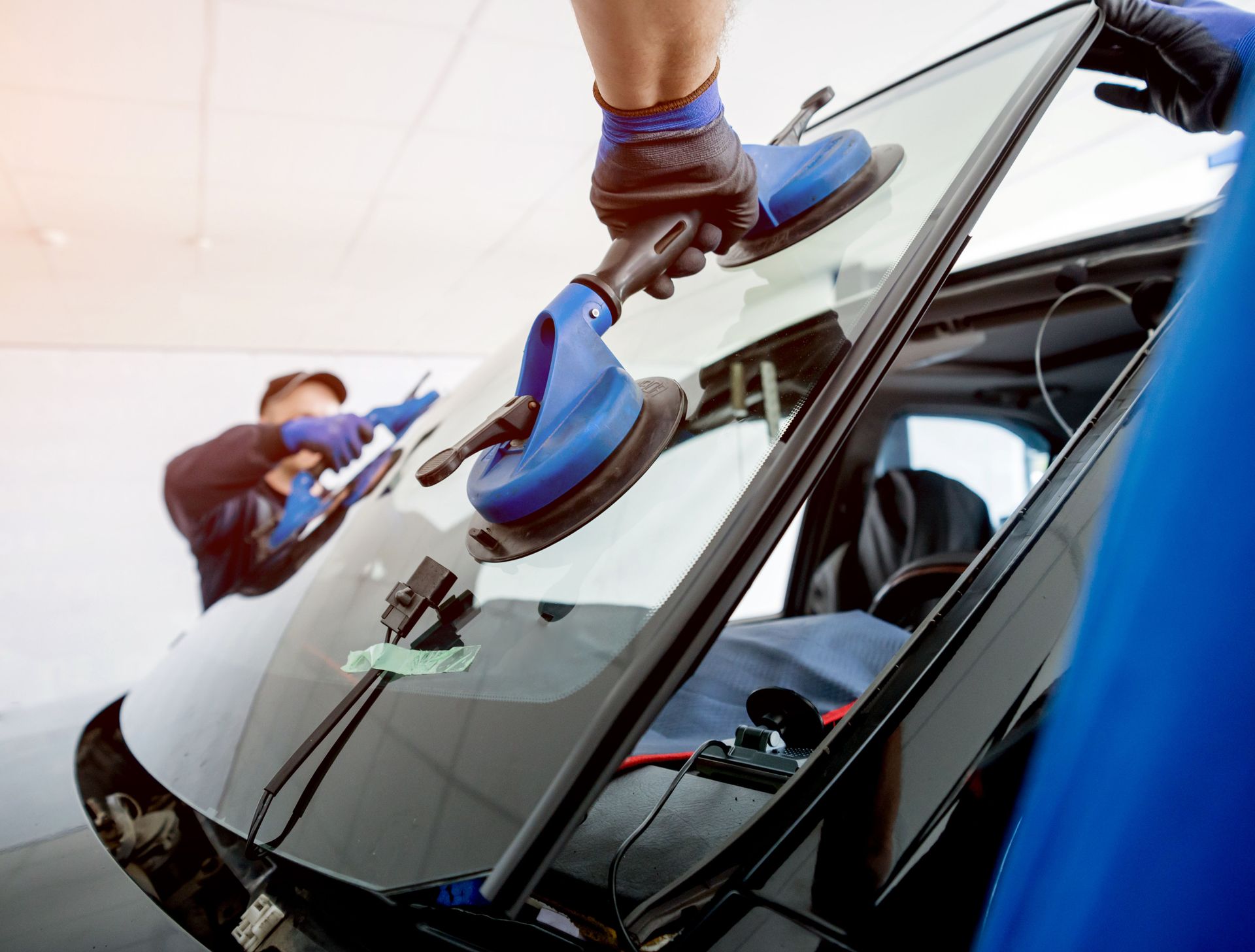 Auto glass specialists fitting a windshield into place with blue suction cup tools.