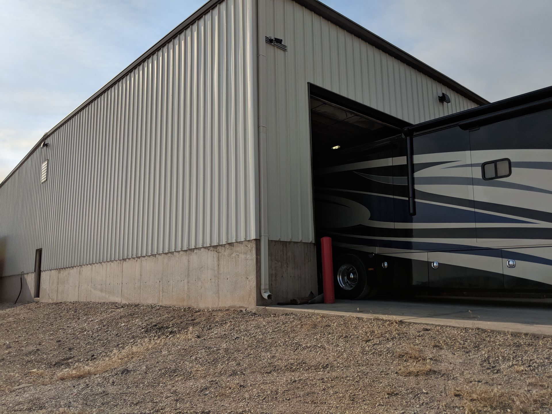 Large RV partially inside a metal warehouse building with roll-up doors.