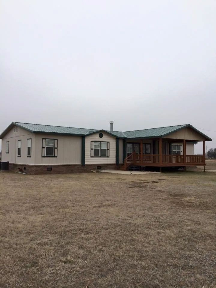 A mobile home with a green roof is sitting in the middle of a field.