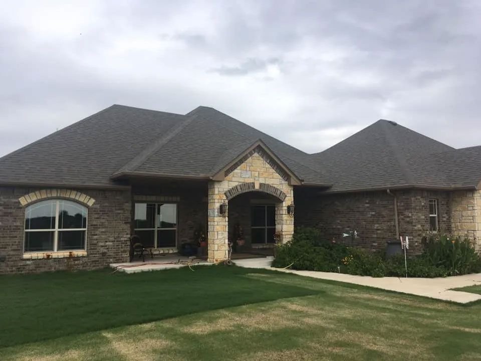 A large brick house with a gray roof and a large lawn in front of it.