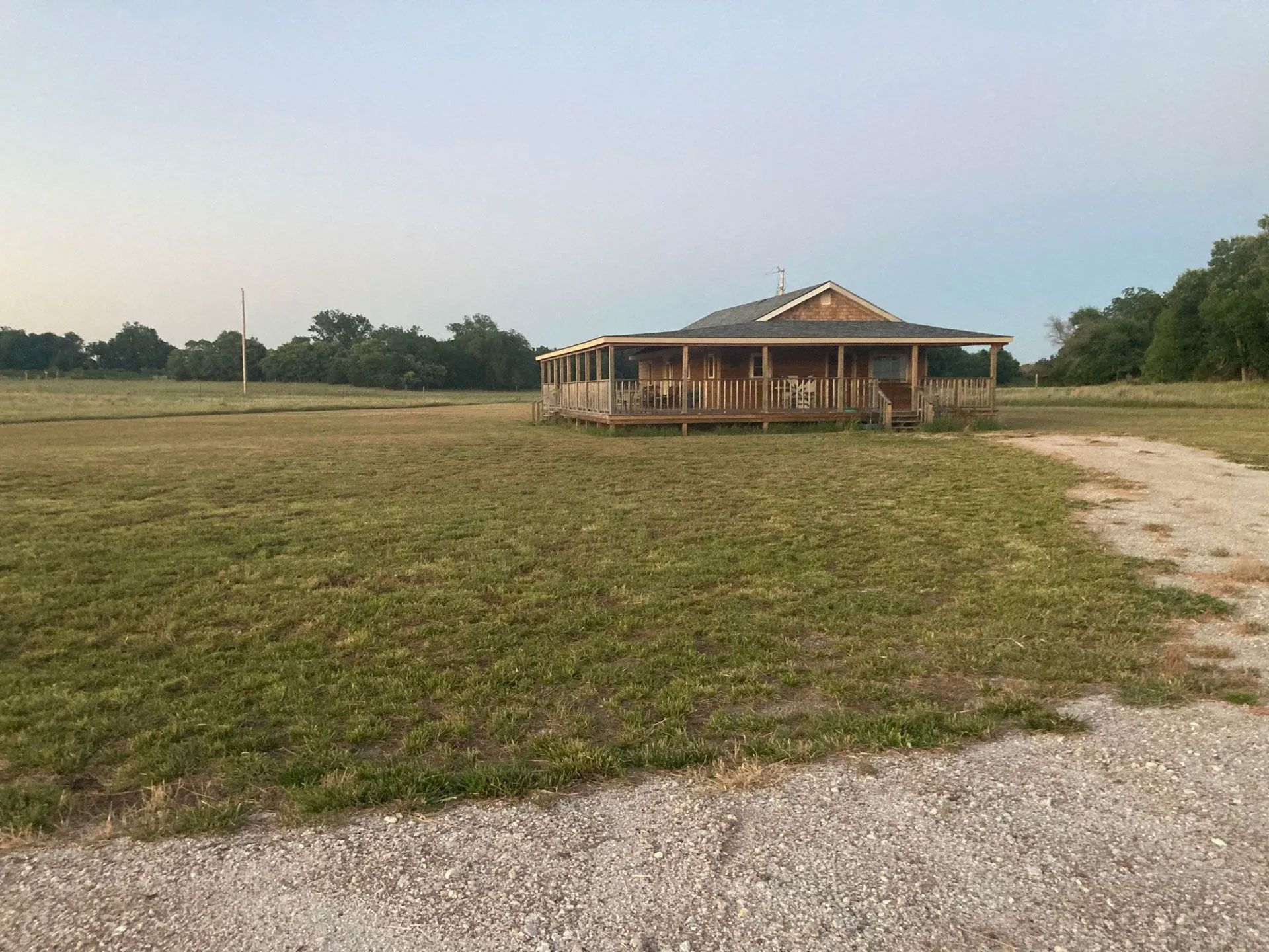 A house with a porch is sitting in the middle of a grassy field.