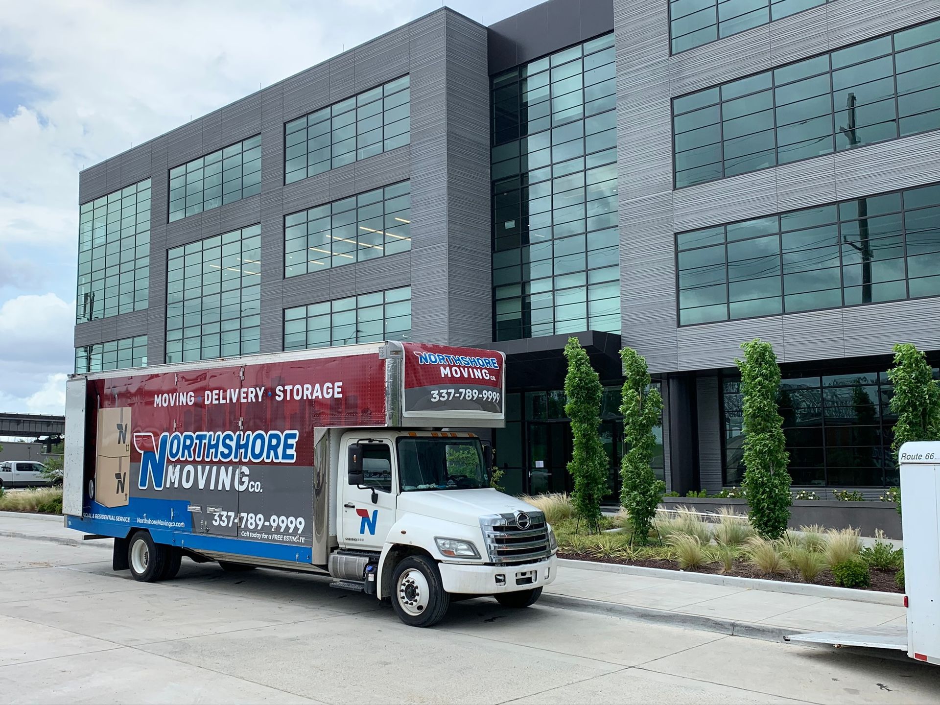 A Northshore Moving truck parked in front of a modern, multi-story office building with a dark brick and glass facade.