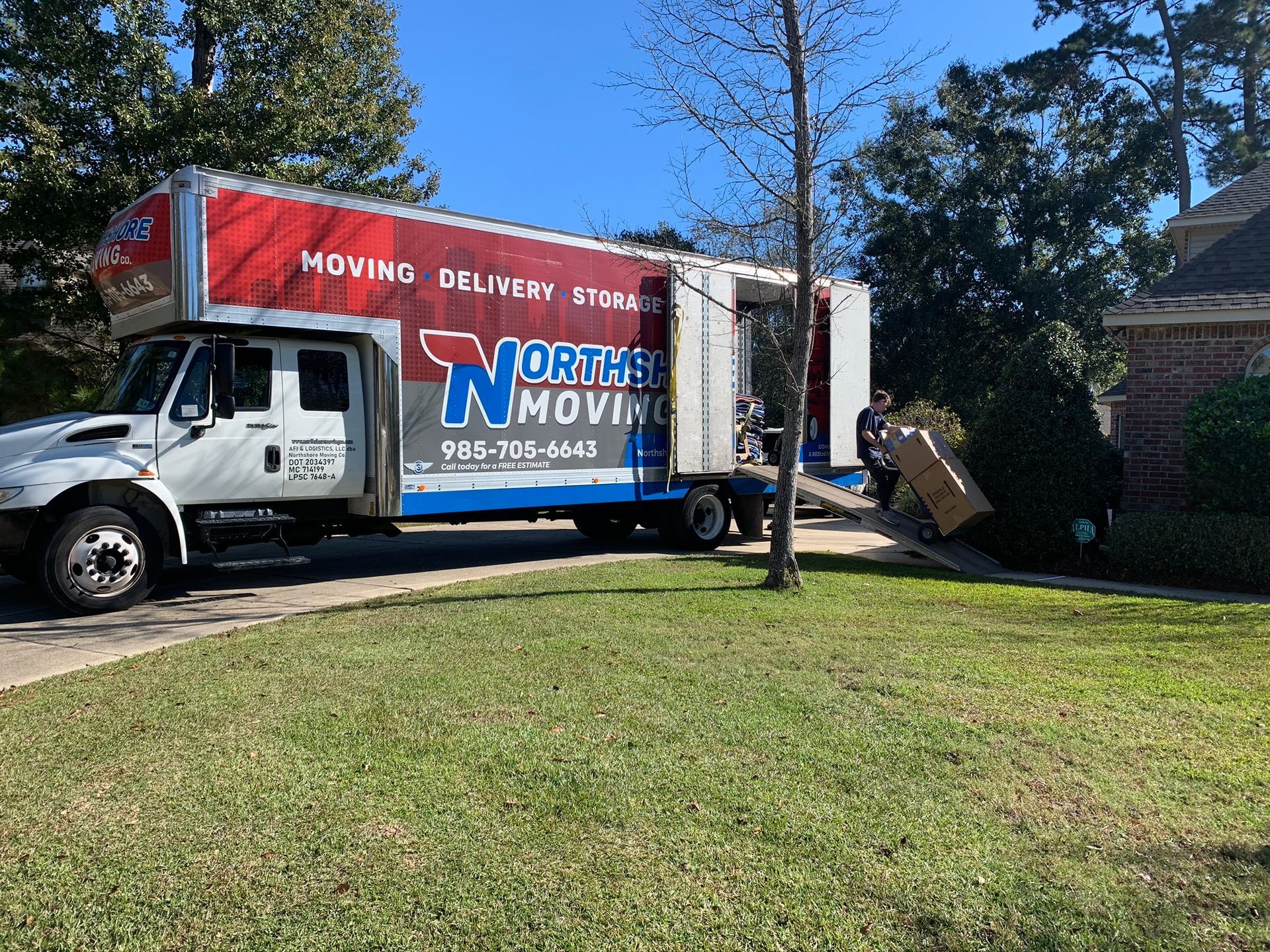 A Northside Moving truck parked on a residential driveway as a person carries a box toward a house.