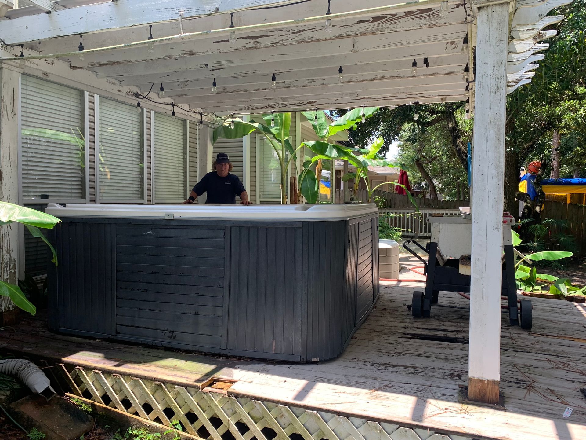 Covered backyard patio with a large gray hot tub and a person standing behind it