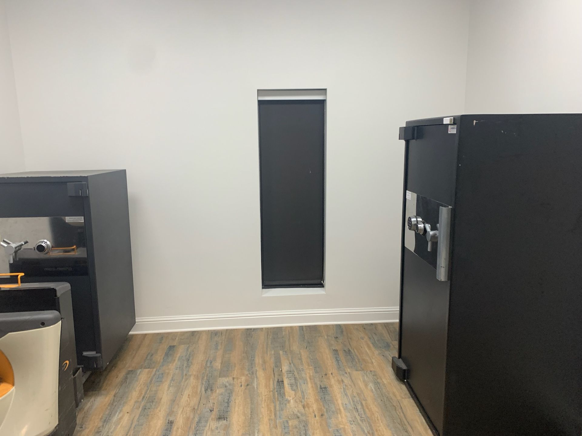 Two large black safes stand on a wood-look floor in a white room with a single narrow window.