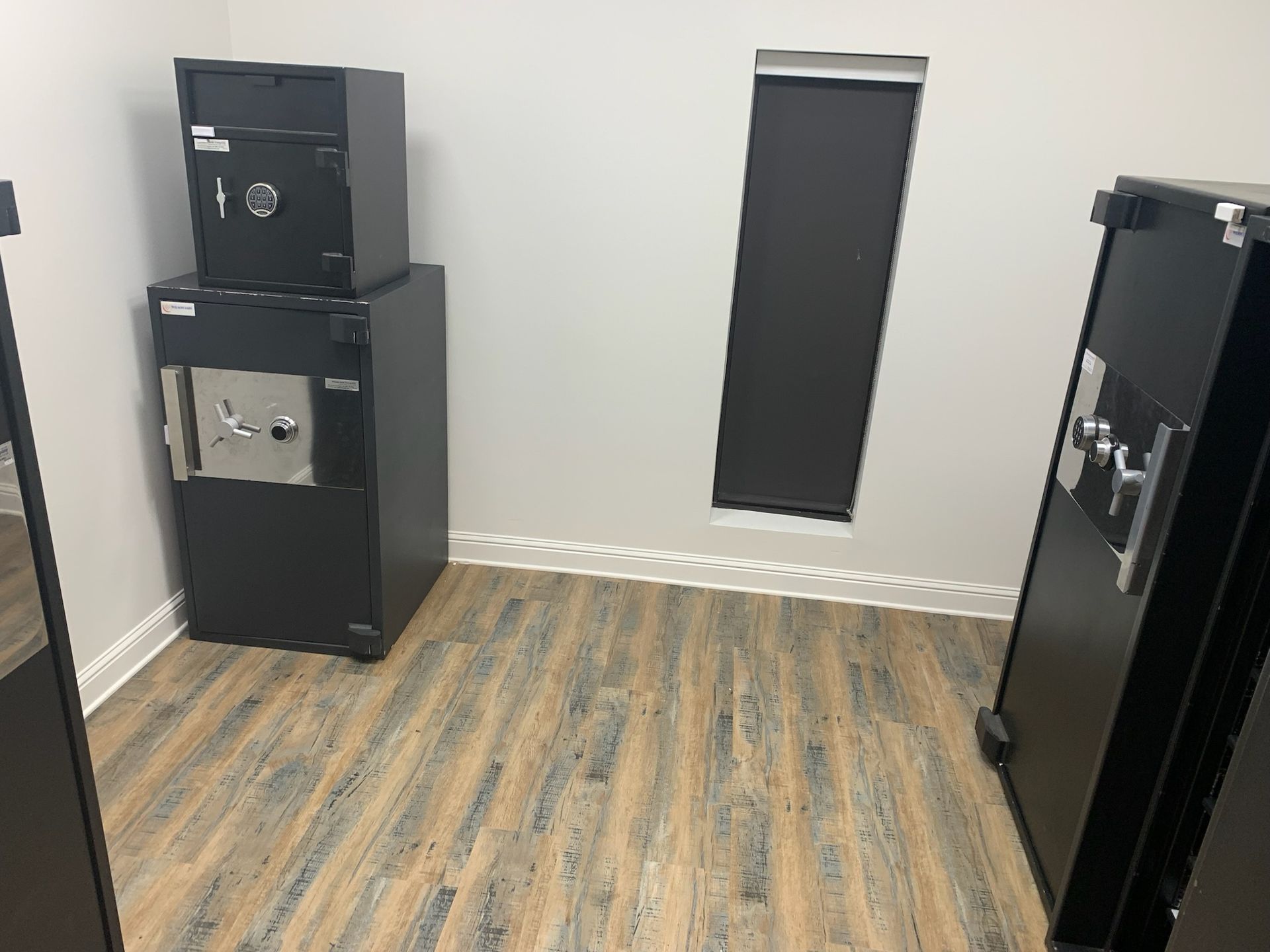 Two black safes stacked on the left, and a large black safe on the right in a room with wood-patterned flooring.