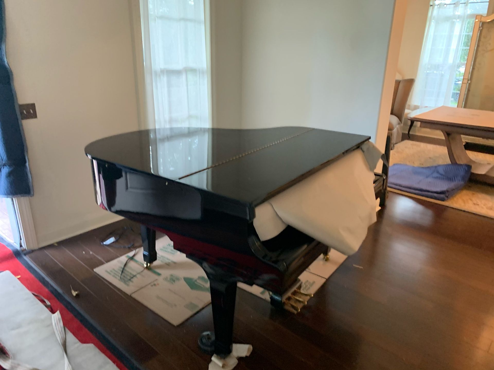 A black grand piano with a partially open lid covered by a light-colored cloth, situated in a room with hardwood floors.