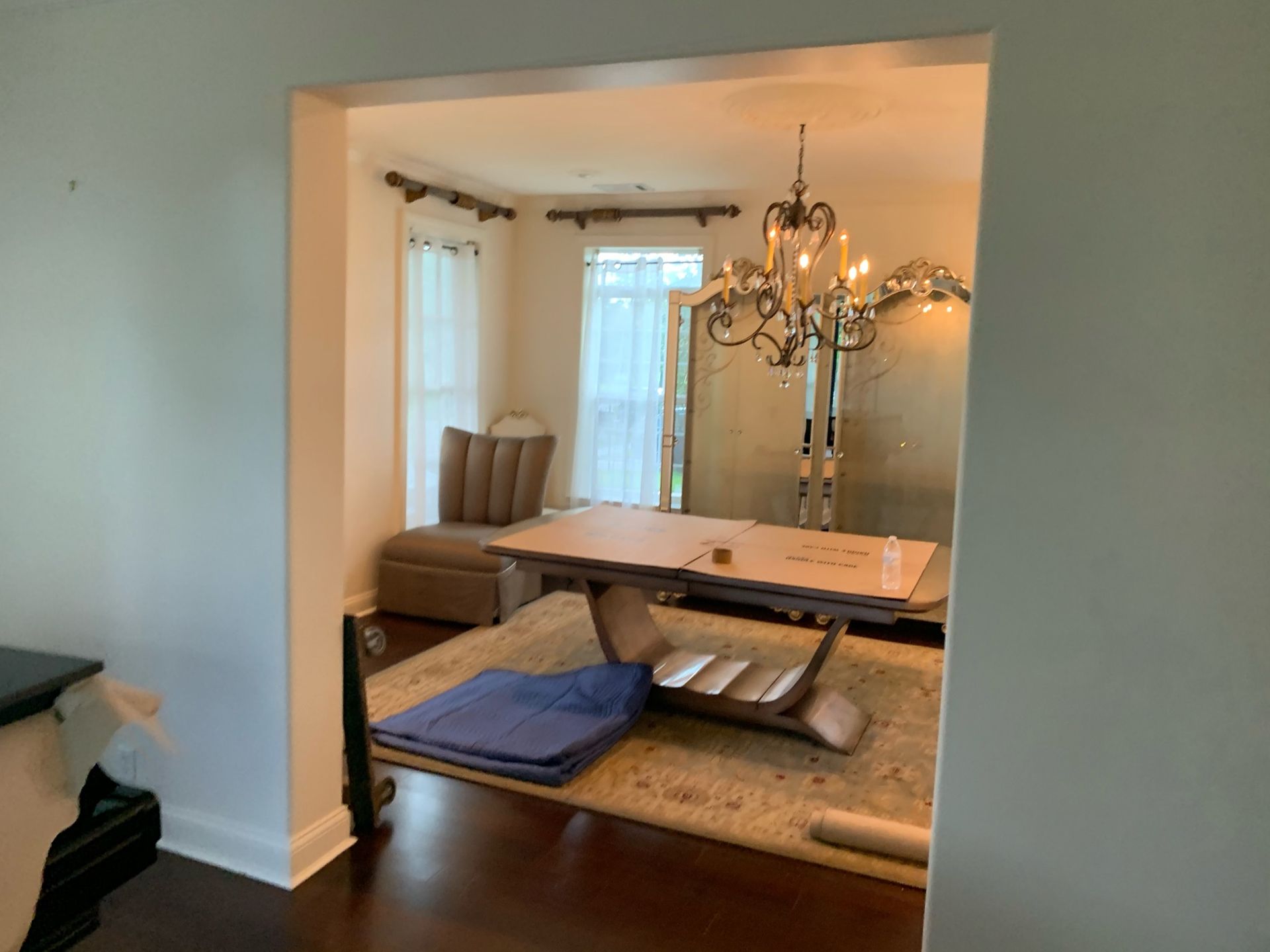 A dining room seen through a doorway, featuring a modern table, a rug, a plush chair, and a crystal chandelier.