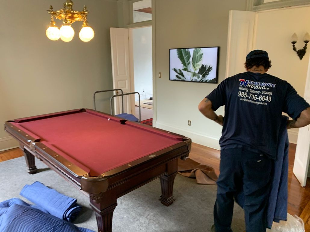Person in a dark shirt stands by a red pool table in a bright living room.