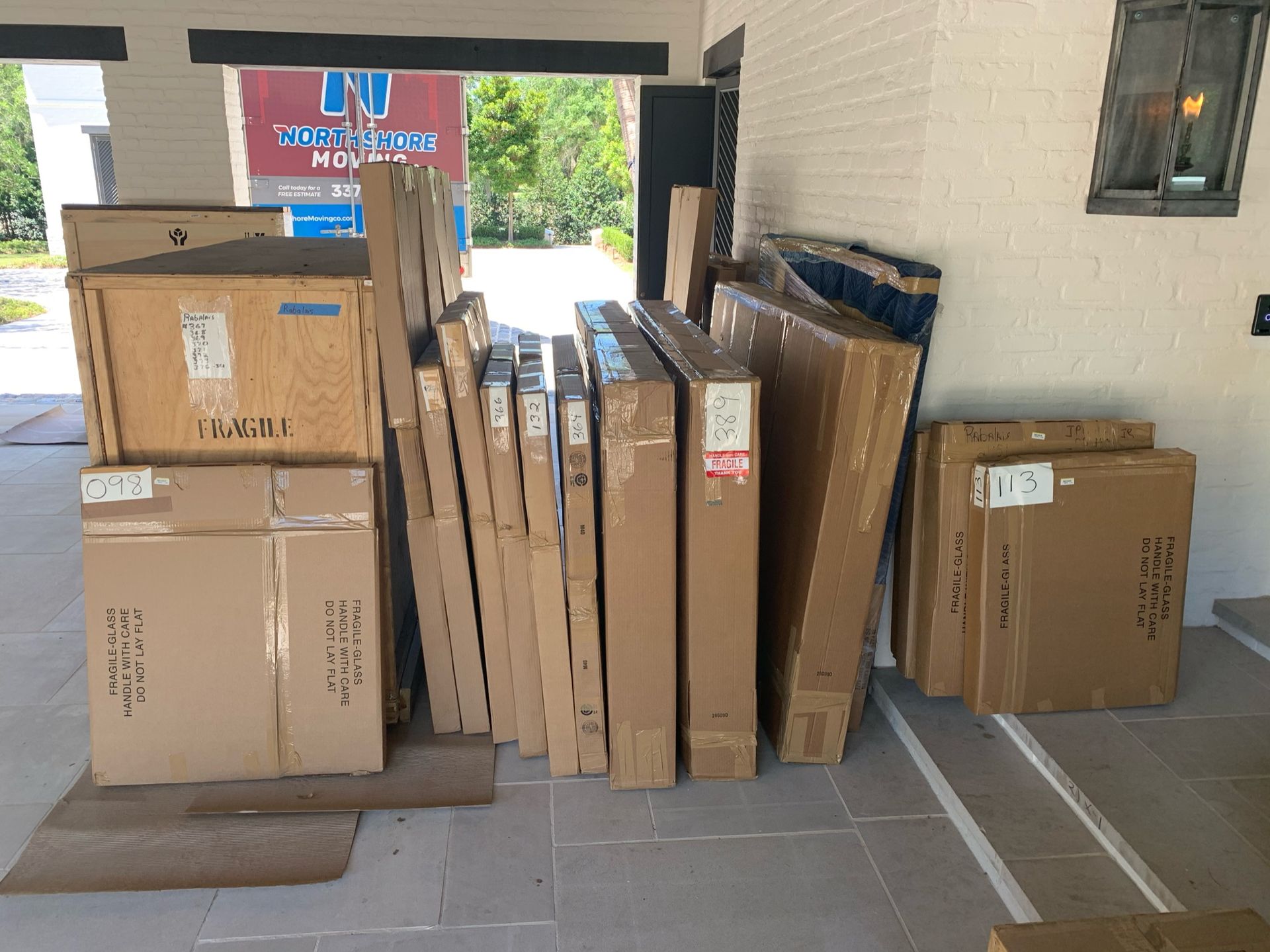 Multiple cardboard shipping boxes, including large rectangular containers and square parcels, are stacked on a patio.