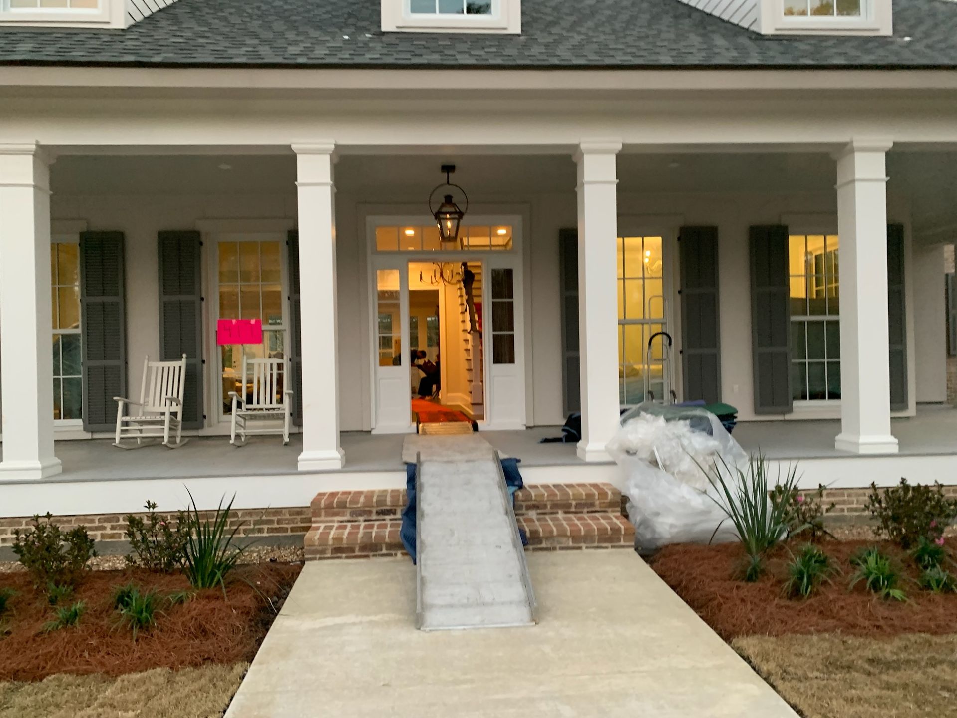 A front porch with white columns, two chairs, and a metal wheelchair ramp leading up to the entrance door.