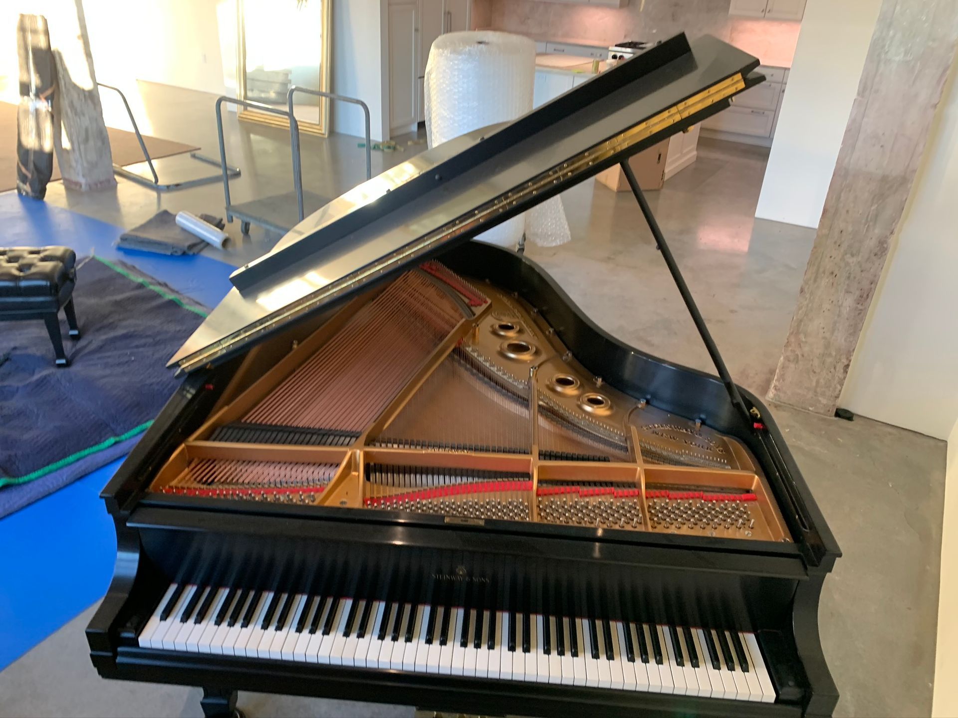 A black grand piano with its lid open, standing on a light-colored floor in a room under renovation.