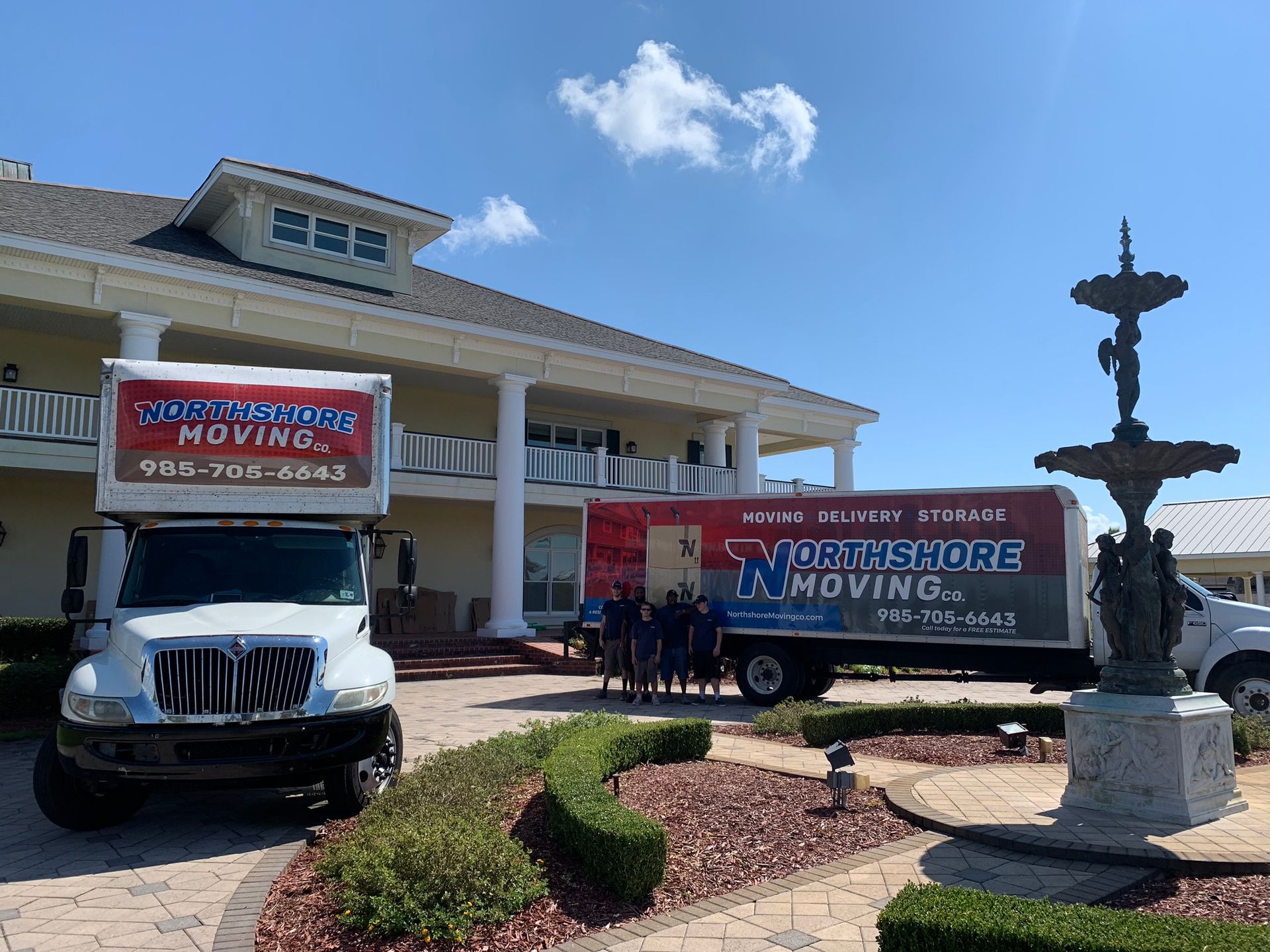 Two Northshore Moving trucks parked in front of a large house with a fountain in the foreground.
