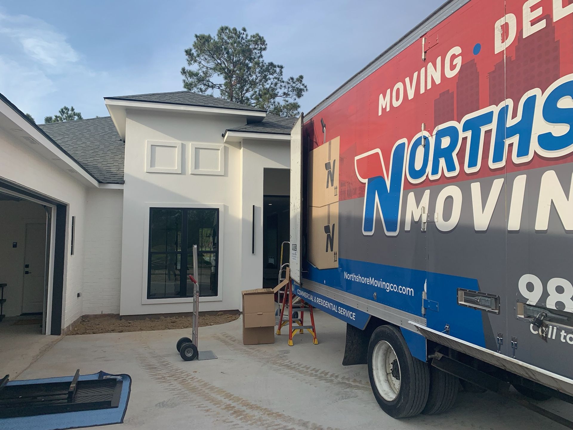 A Northside Moving truck parked in the driveway of a white house, with a dolly and cardboard boxes near the entrance.