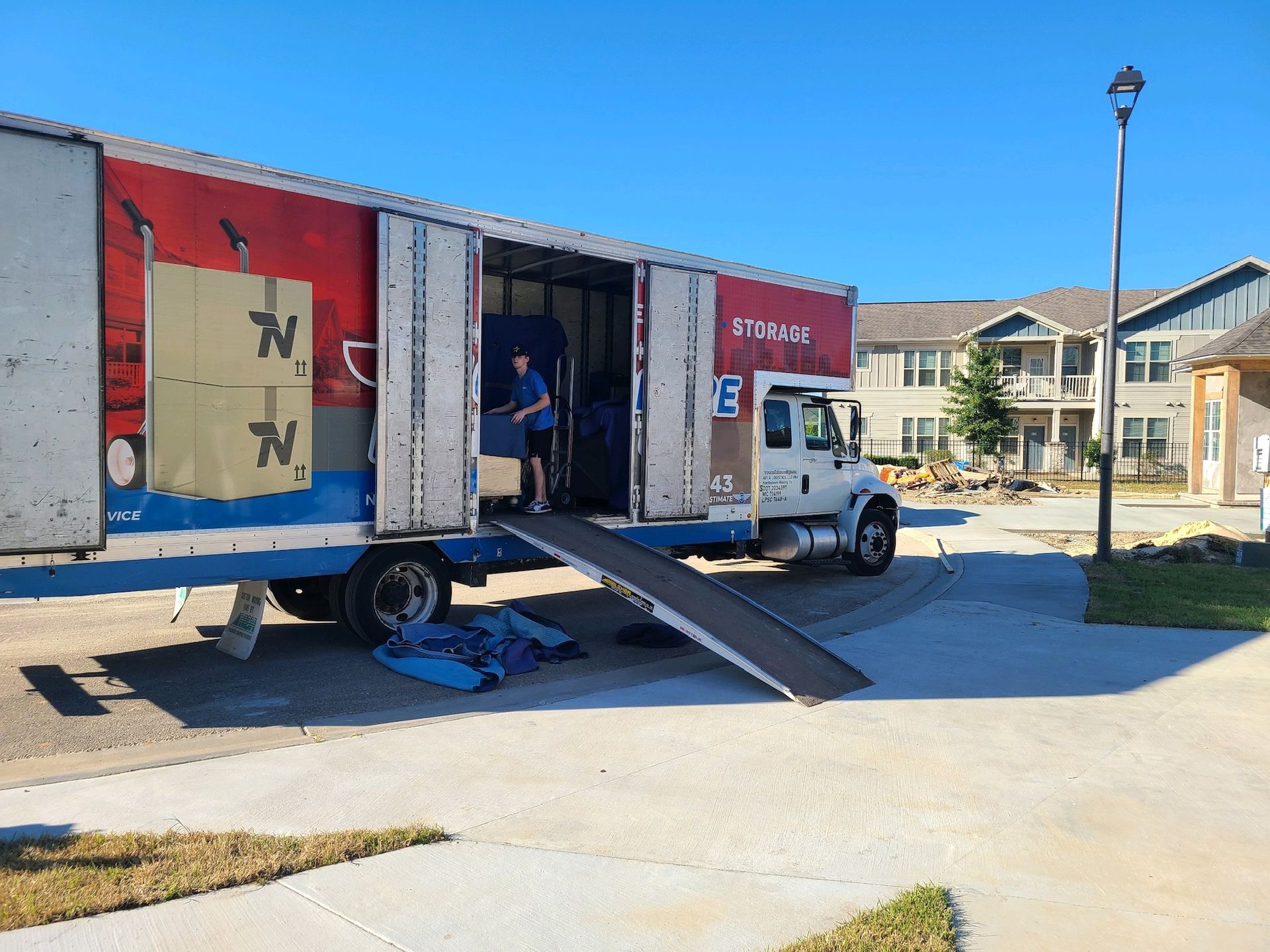 A moving truck parked on a sunny day with its loading ramp down and a person inside the cargo area.